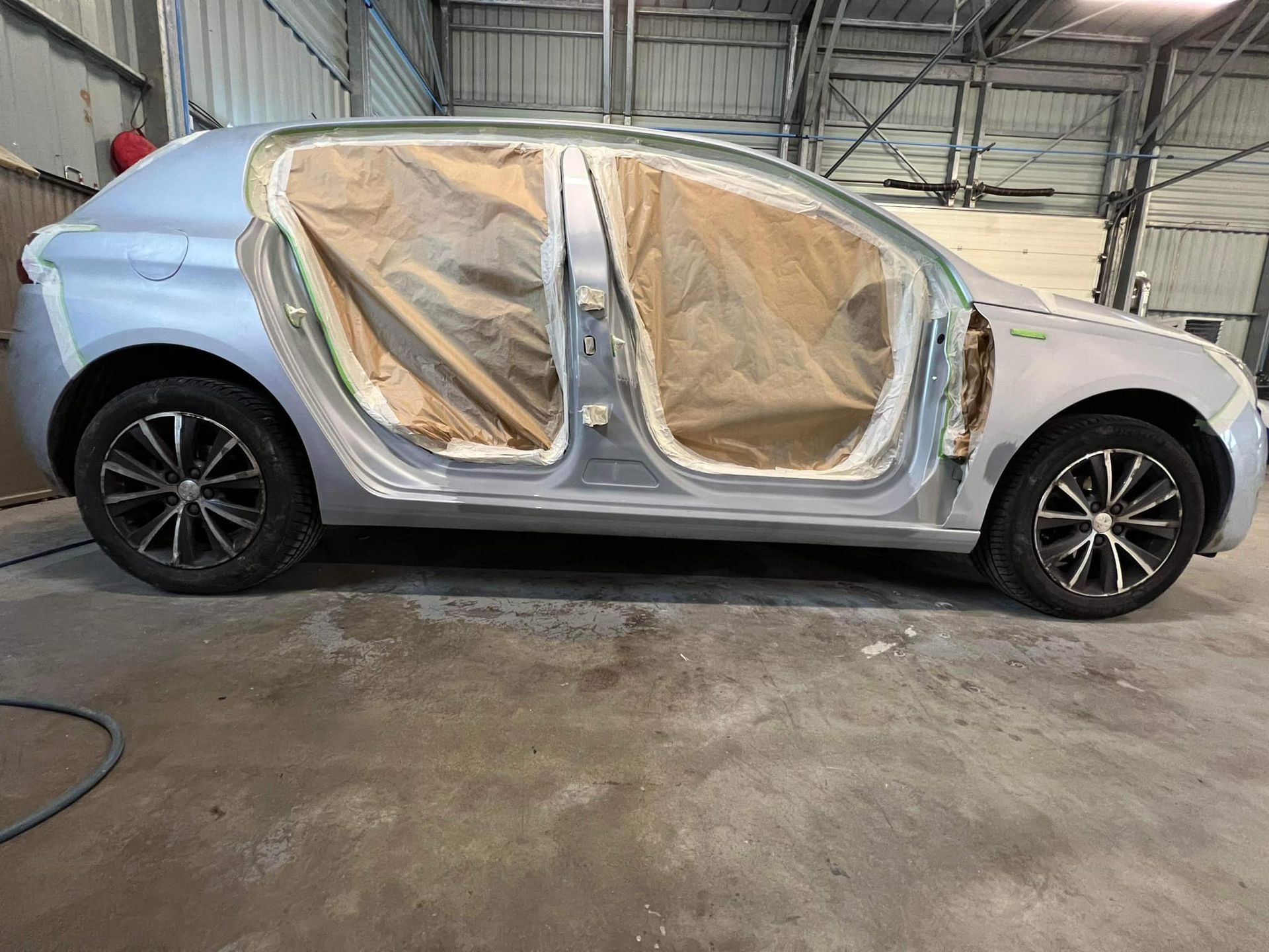 Voiture dans un atelier de réparation automobile ; portes masquées, carrosserie préparée pour la peinture.