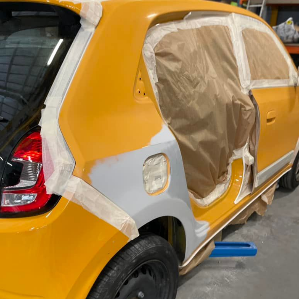 Voiture jaune, panneau arrière apprêté pour la peinture, masqué avec du ruban adhésif, porte ouverte.
