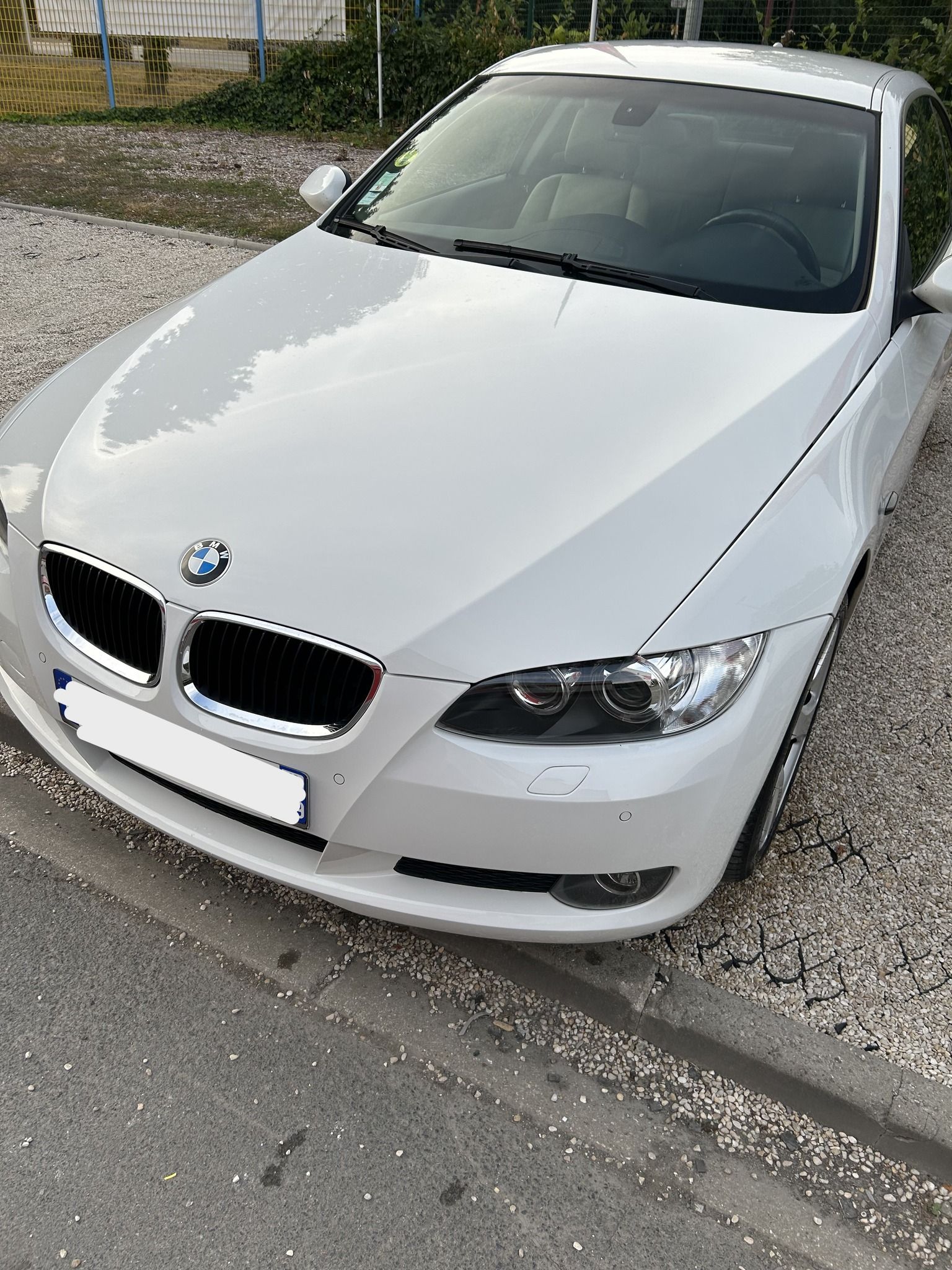 Berline blanche garée sur le bord d'une route, vue de face.