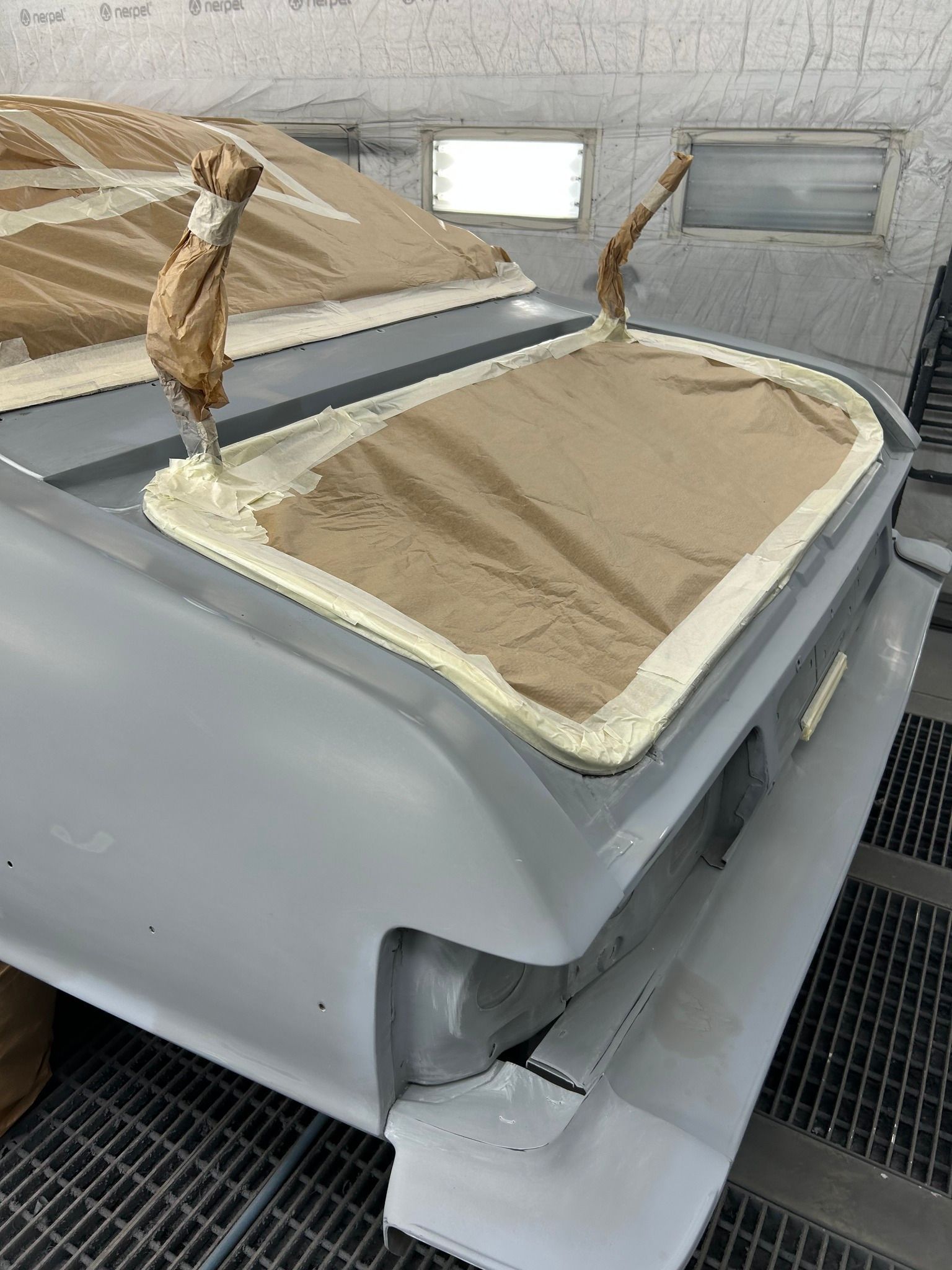 Coffre de voiture partiellement peint, masqué pour les détails ; gris clair, papier de masquage beige. Intérieur d'un atelier.