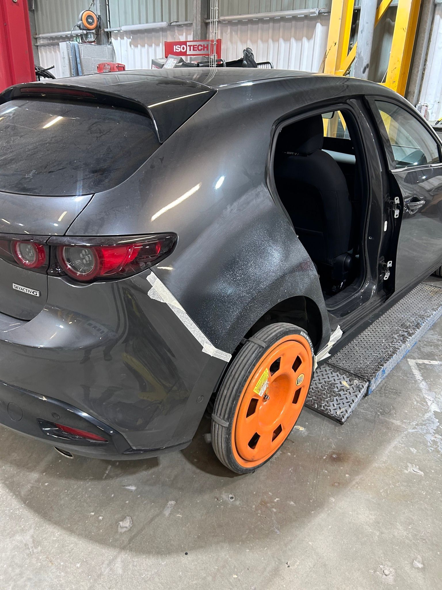 Voiture à hayon gris foncé dans un atelier de réparation automobile, panneau arrière endommagé, enjoliveur orange.
