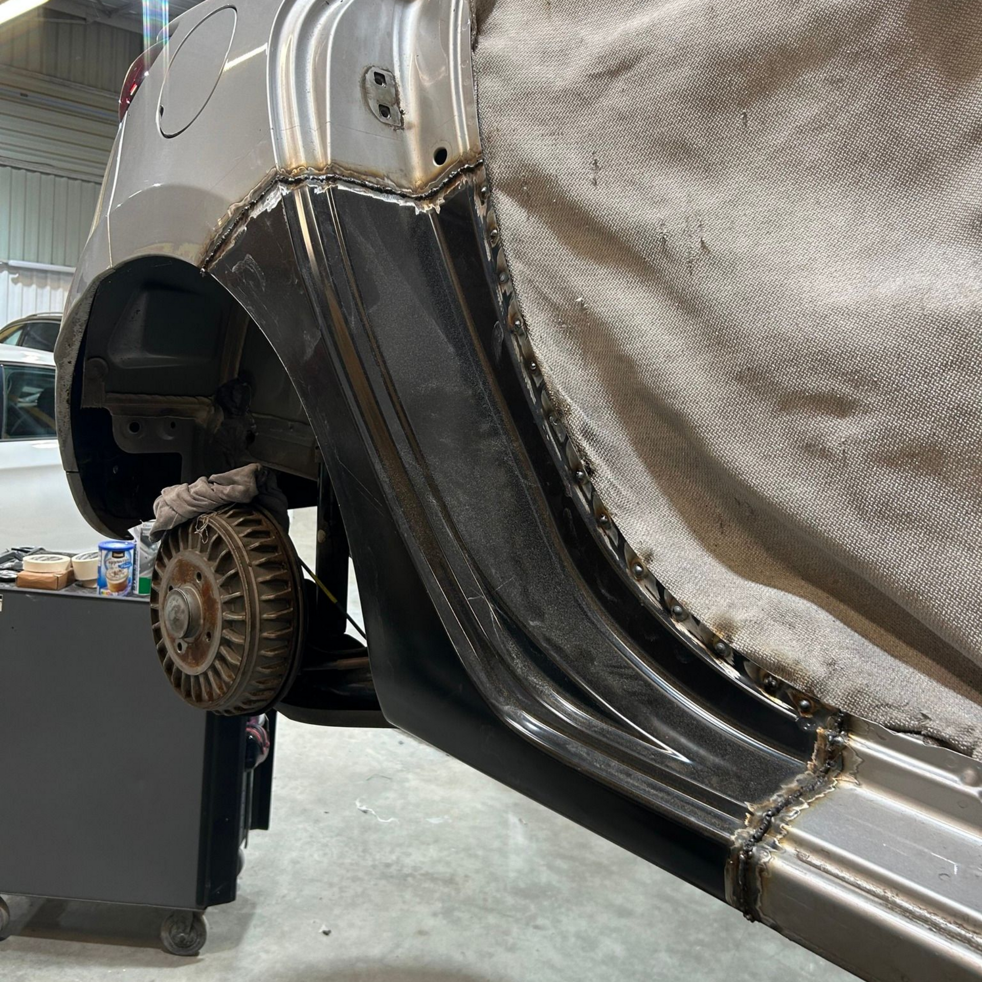 Soudure sur le bas de caisse d'une voiture. Un panneau métallique est soudé sur le côté de la voiture. Un tissu gris protège l'intérieur.