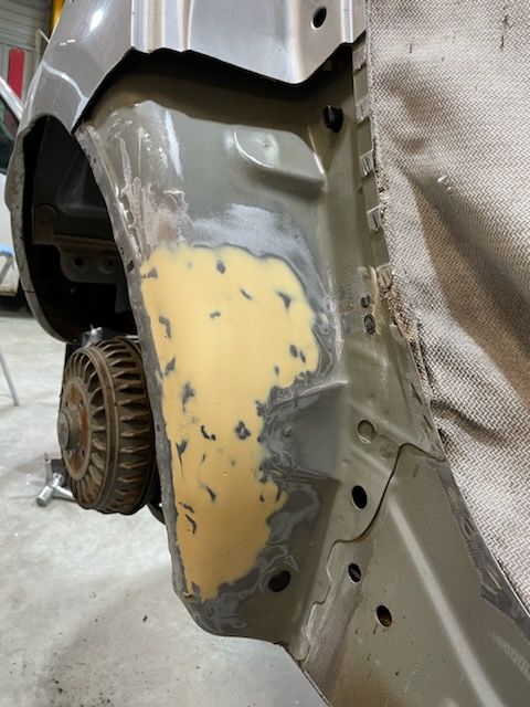 Panneau de carrosserie réparé avec du mastic. Des couleurs beige, grise et argentée sont visibles.