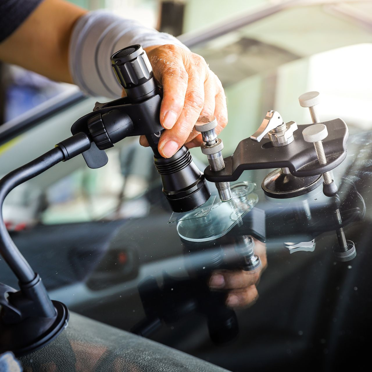Personne réparant un pare-brise de voiture fissuré avec des outils de réparation.
