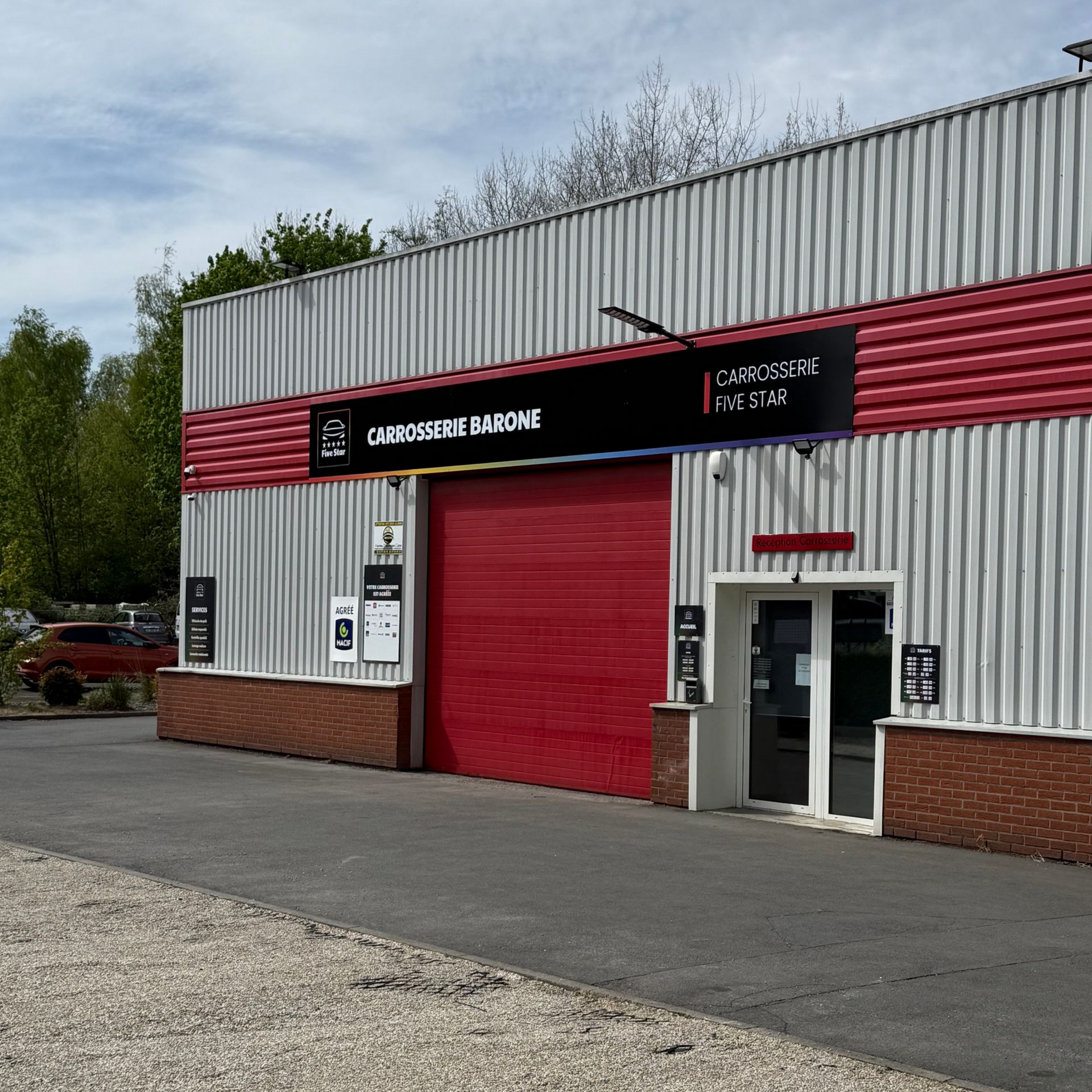 Extérieur du garage avec une porte rouge et une enseigne Carrosserie Barone.