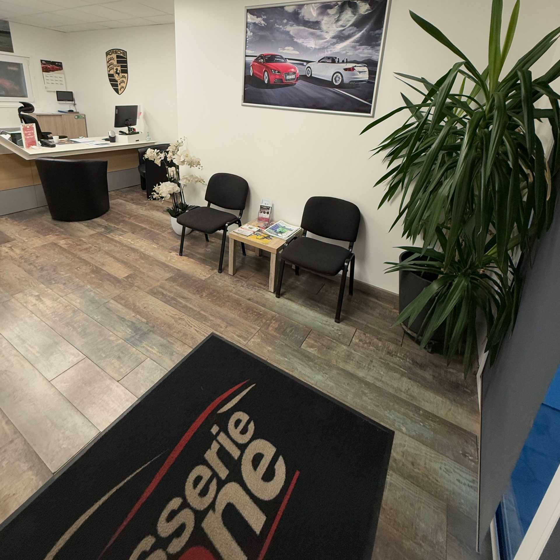 Espace de réception avec deux chaises noires, une petite table et une grande plante.