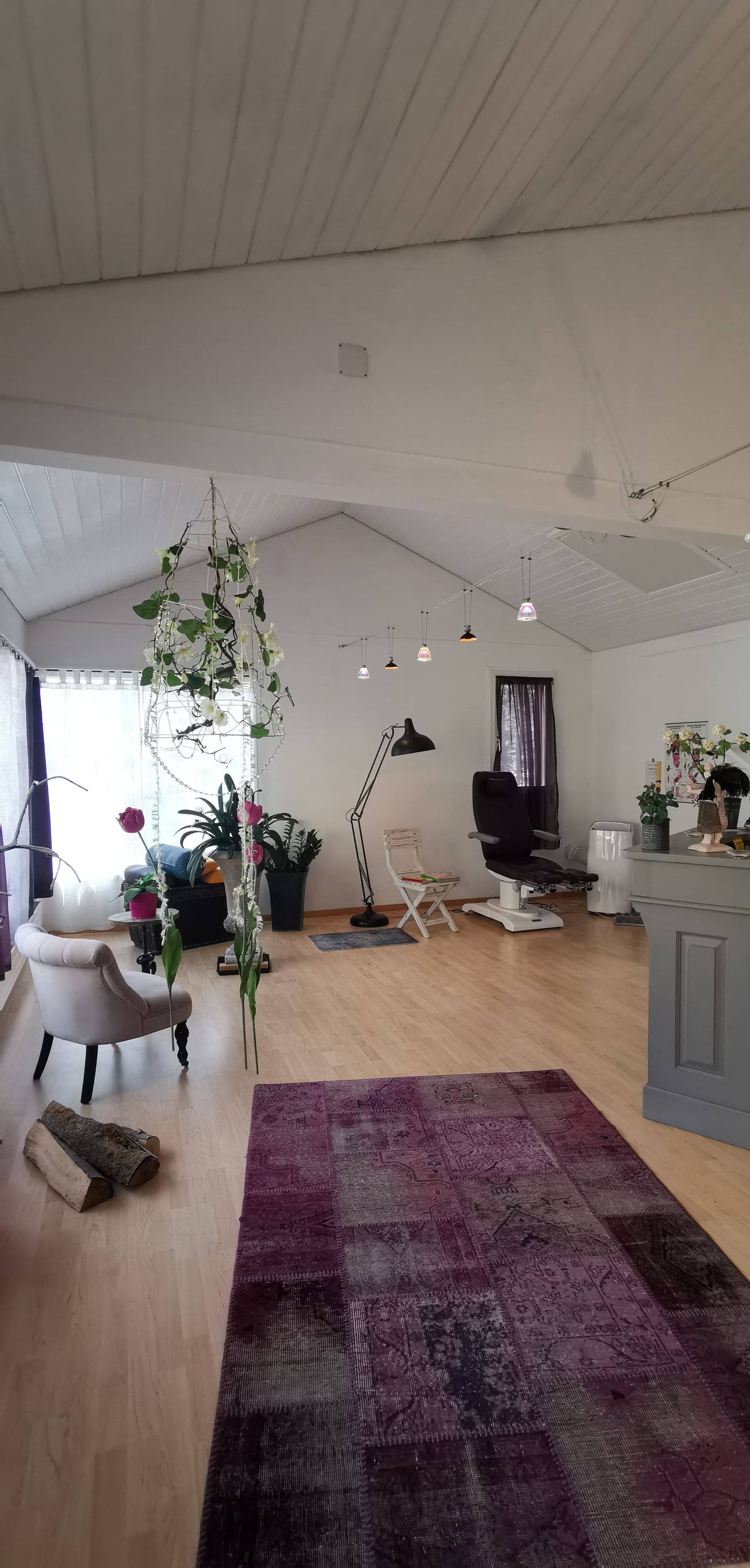 Heller Raum mit Holzböden, lila Teppich, weißen Wänden und dekorativen Pflanzen.