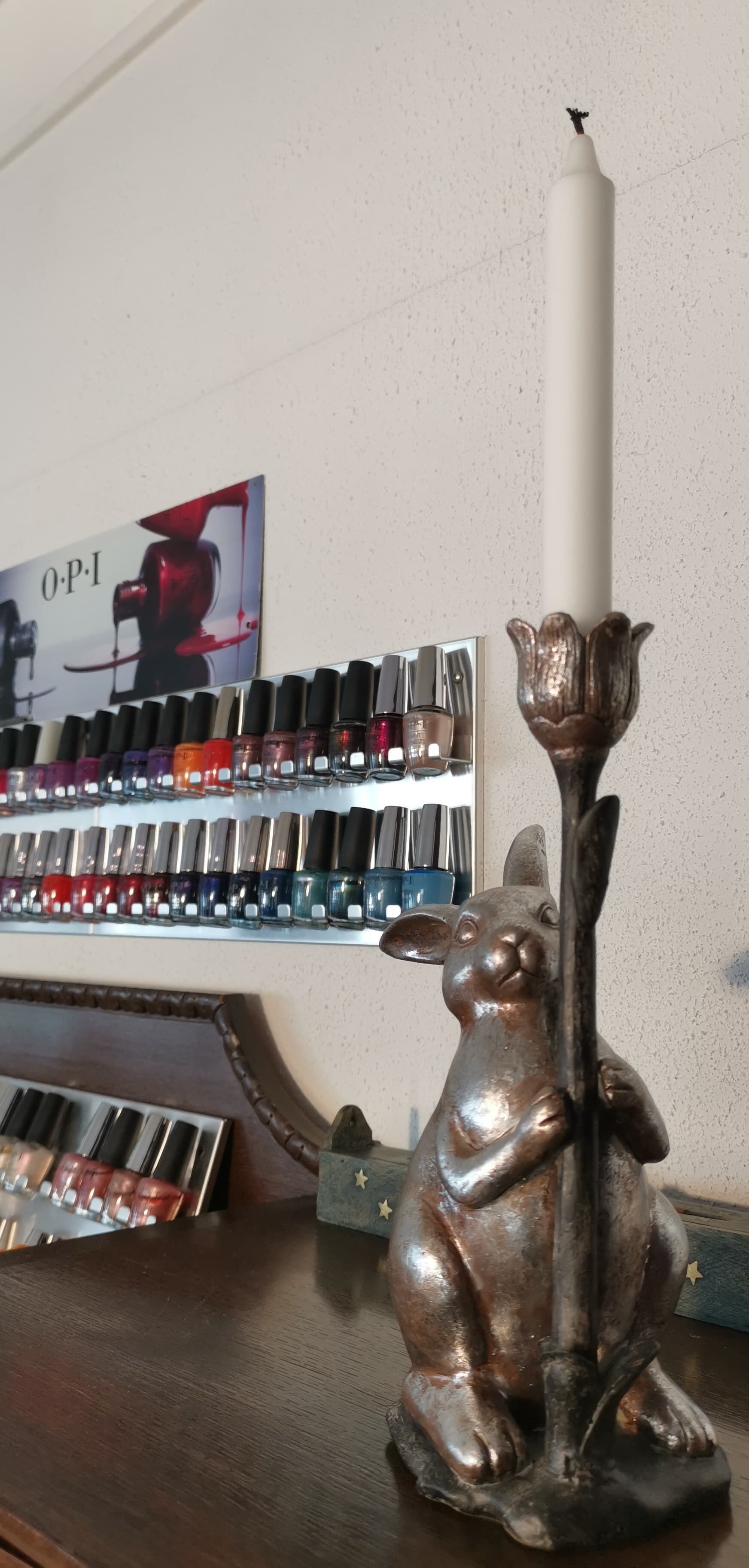 Kerze in einem kaninchenförmigen Halter auf einer Holzoberfläche, Nagellackflaschen im Hintergrund.