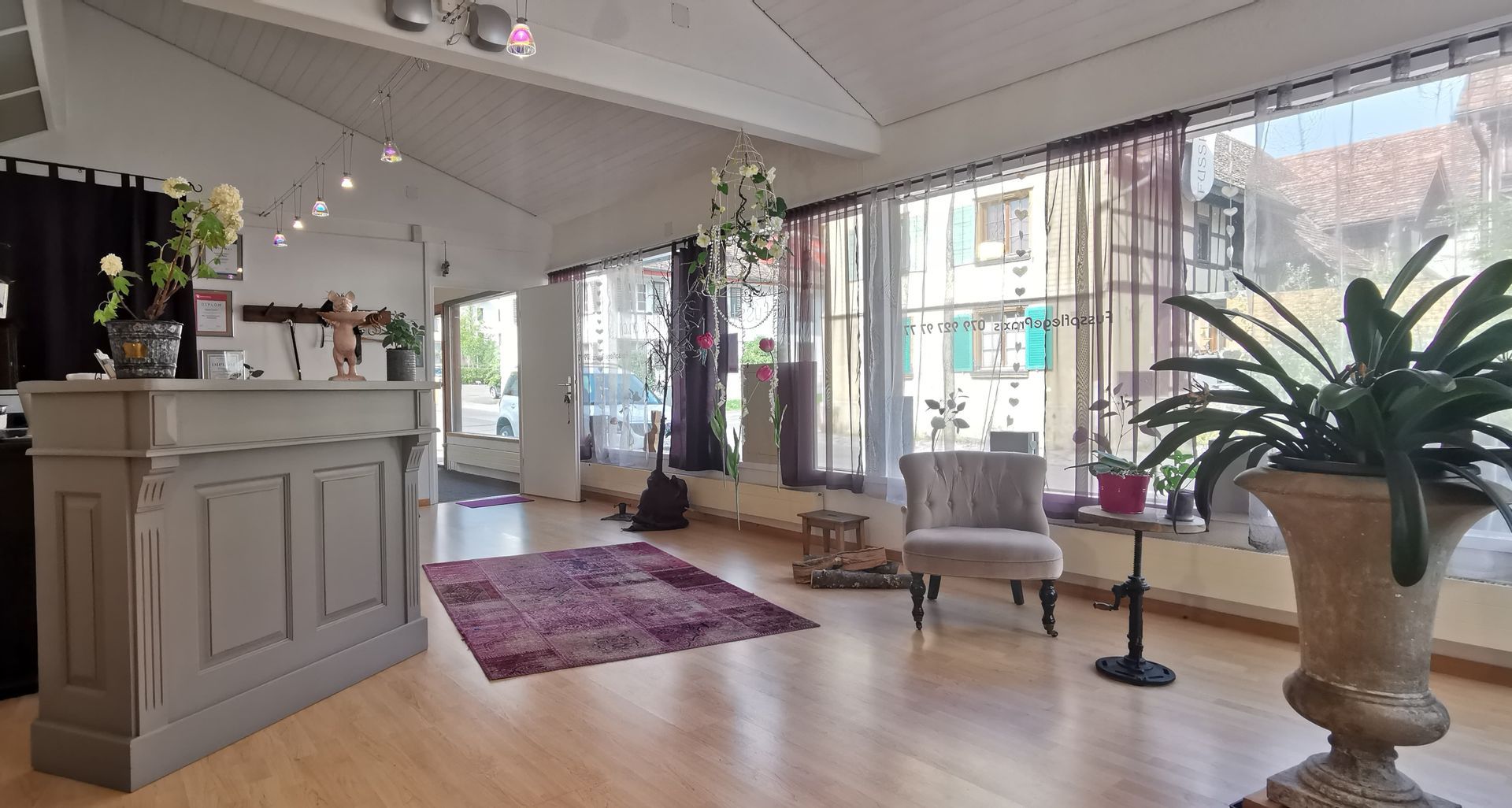 Helles Interieur mit Rezeption, Fenstern, gemustertem Teppich, Stuhl und Pflanzen; möglicherweise ein Studio oder Geschäft.