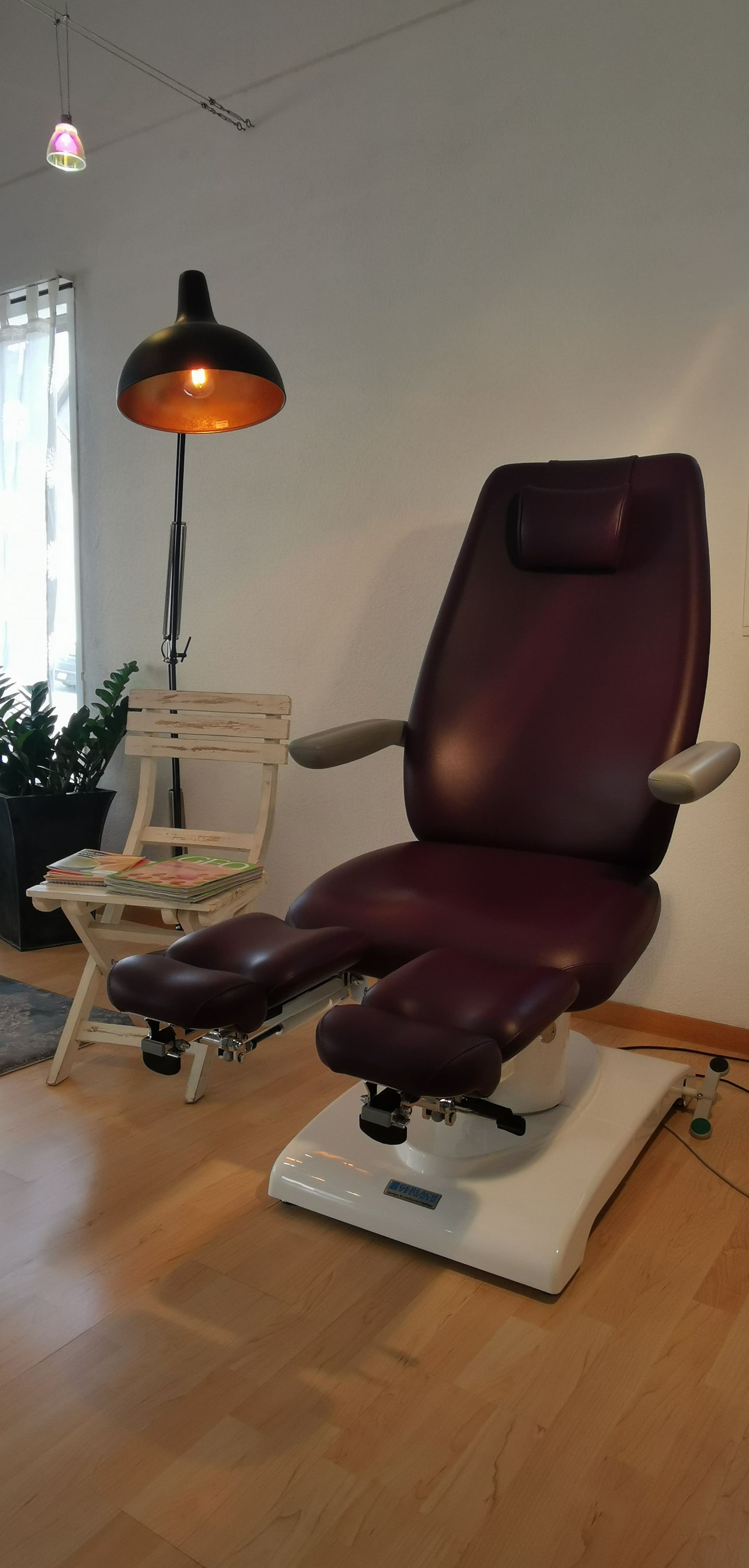 Ein medizinischer Stuhl in einem Raum mit einer Lampe, einer weißen Wand und einem Holzboden.