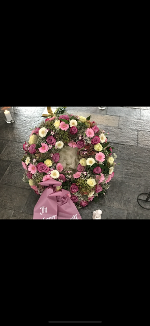 Ein Blumenkranz mit rosa und weißen Blumen auf einer grau gefliesten Oberfläche.