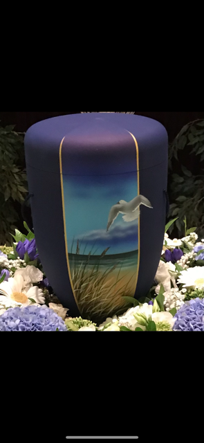 Blaue Urne mit einer gemalten Küstenszene mit einer Möwe, umgeben von Blumen.