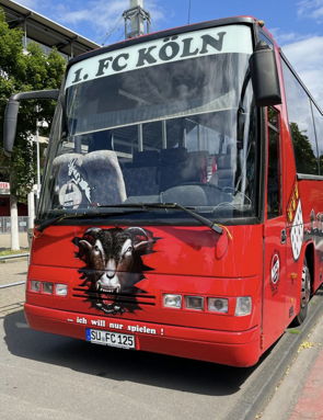 Roter Mannschaftsbus des 1. FC Köln mit Ziegenmotiv, geparkt auf einer Straße.