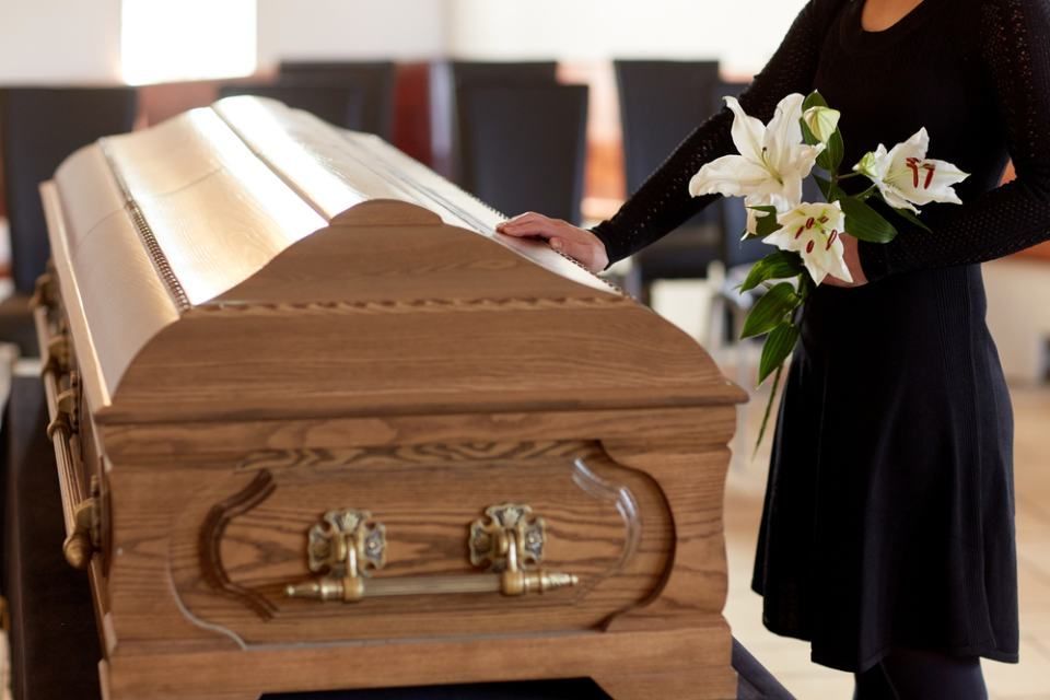 Frau berührt einen Sarg und verabschiedet sich während einer Bestattungszeremonie.