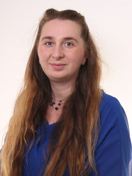 Eine Frau mit langen Haaren trägt ein blaues Hemd und eine Halskette.