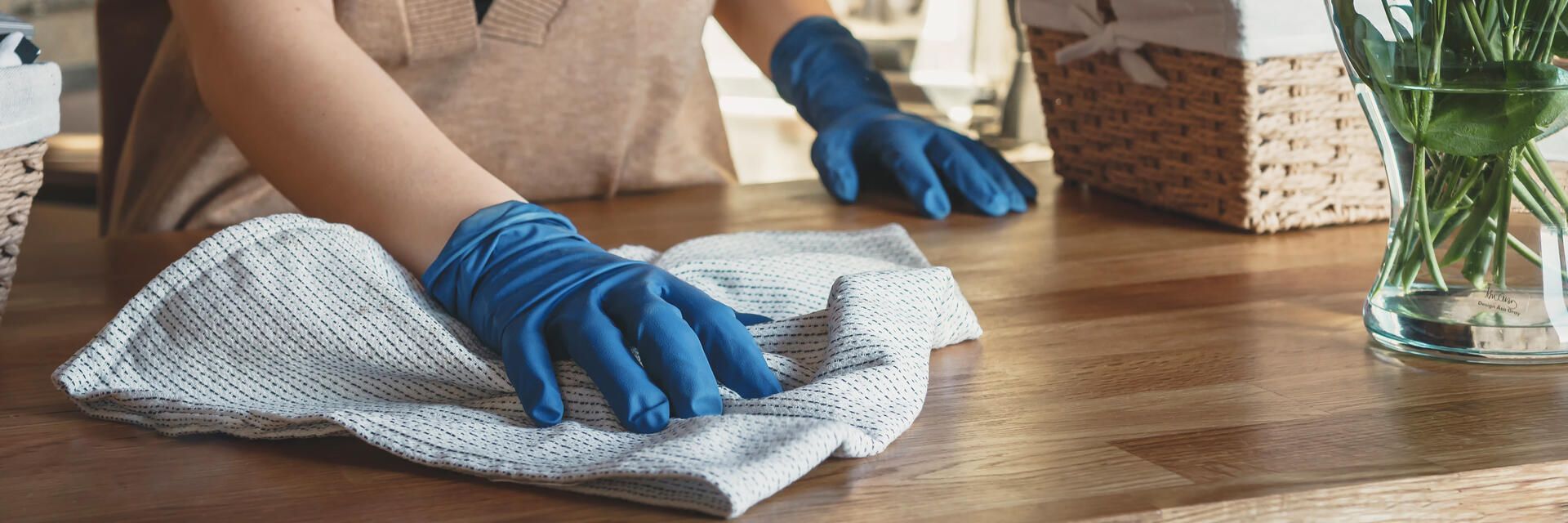 Eine Person mit blauen Handschuhen reinigt einen Holztisch mit einem Handtuch.
