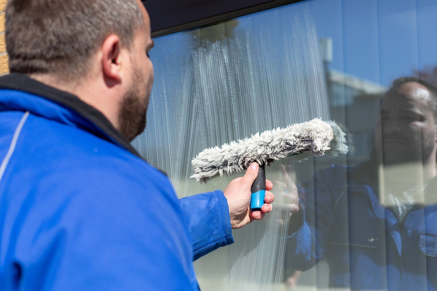 Ein Mann putzt ein Fenster mit einem Abzieher.