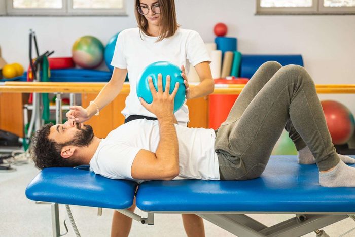Un hombre está acostado sobre una mesa mientras una mujer sostiene una pelota azul sobre su cabeza.