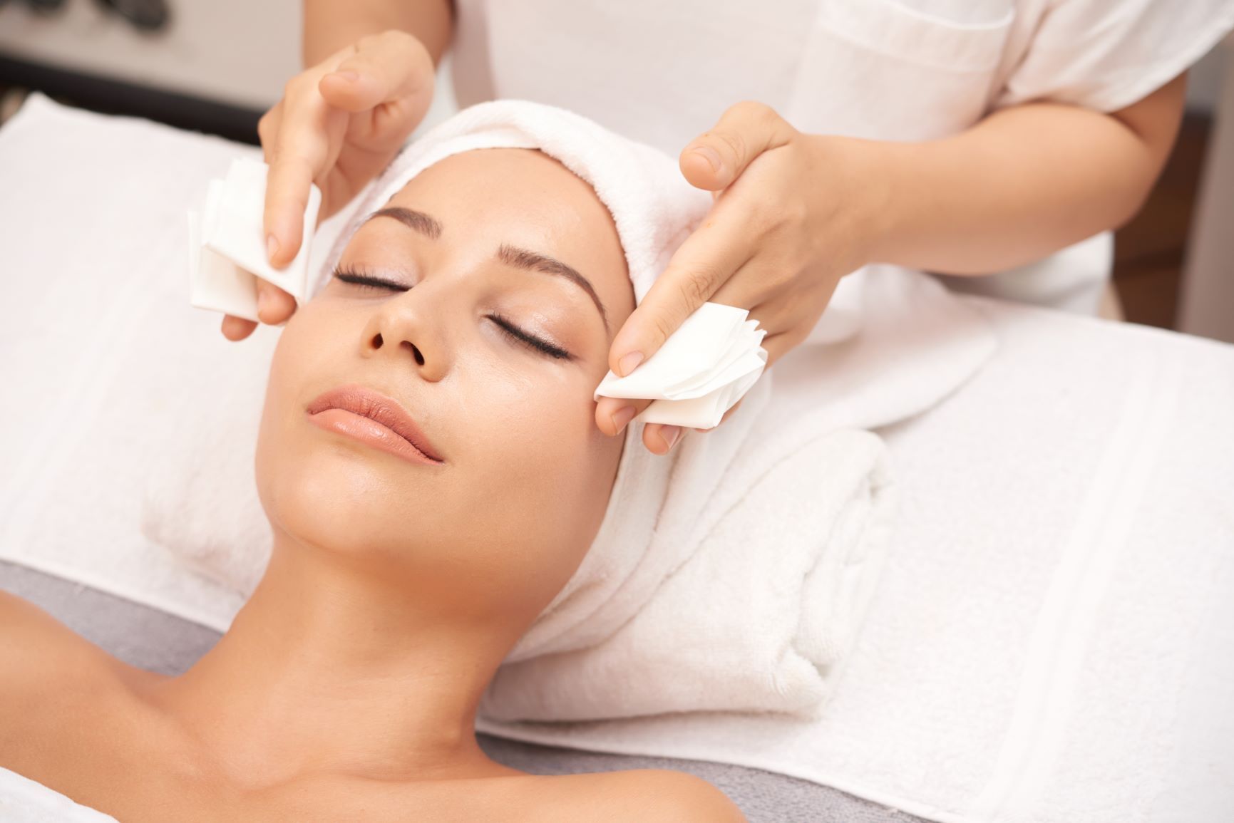 Une esthéticienne applique un soin du visage à une cliente allongée dans un spa.