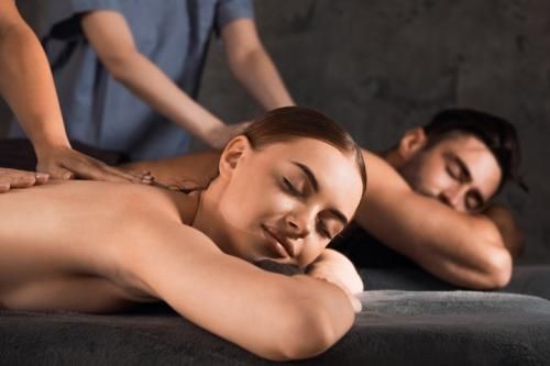 Une personne reçoit un massage du dos dans un spa, allongée à côté d'une autre personne également détendue sur une table de massage.