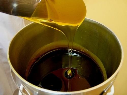 Un liquide épais, jaune doré, est versé dans un récipient métallique partiellement rempli d'un liquide sombre et visqueux.