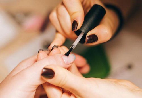 Un professionnel applique une base de vernis transparent sur les ongles d'une personne.