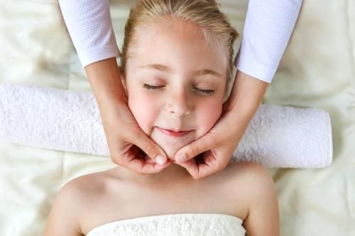 Une personne reçoit un massage facial doux en position allongée, une serviette blanche placée derrière la tête.