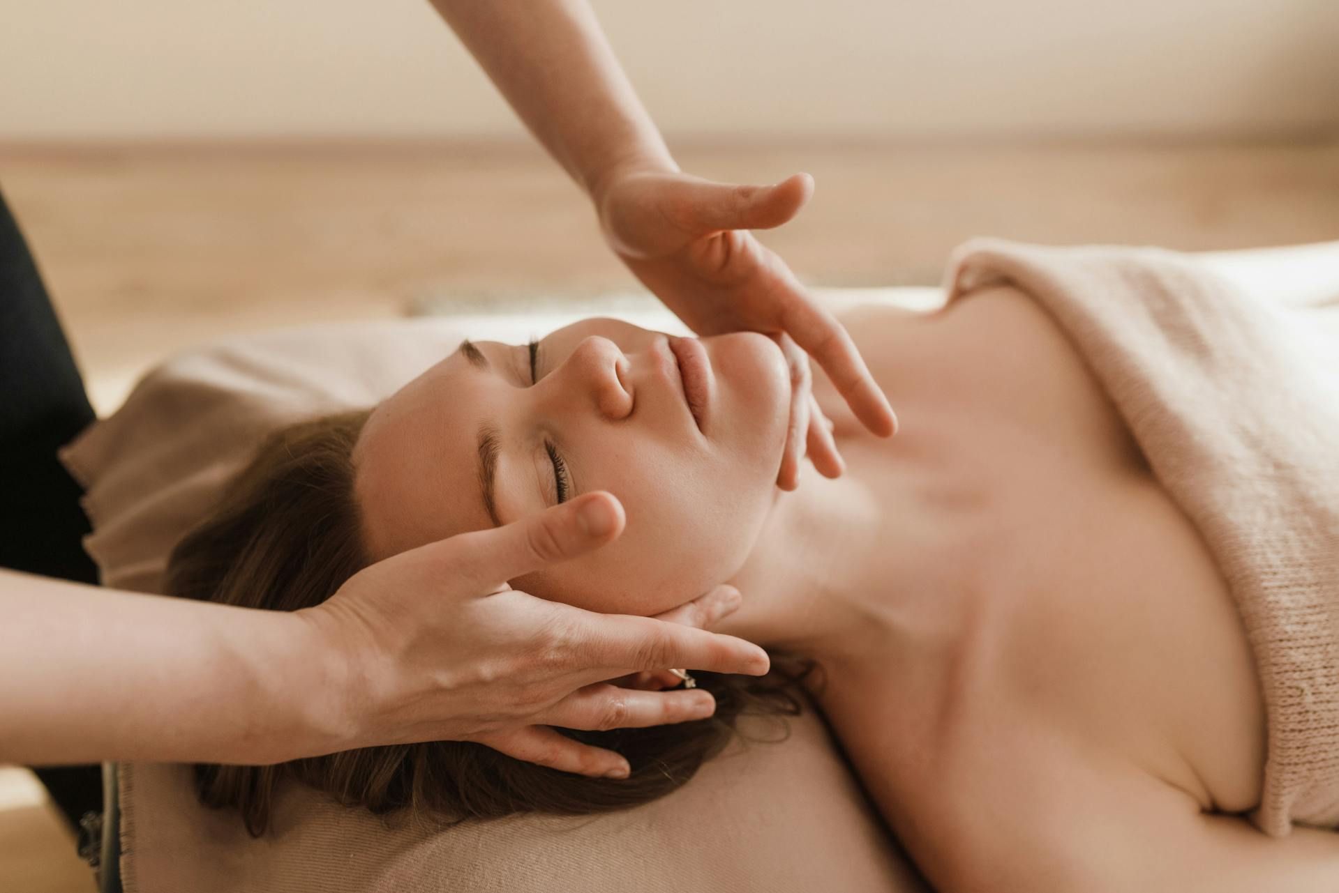 Une personne est allongée sur une table tandis qu'un praticien effectue un massage facial en posant délicatement ses mains sur le front de la personne.