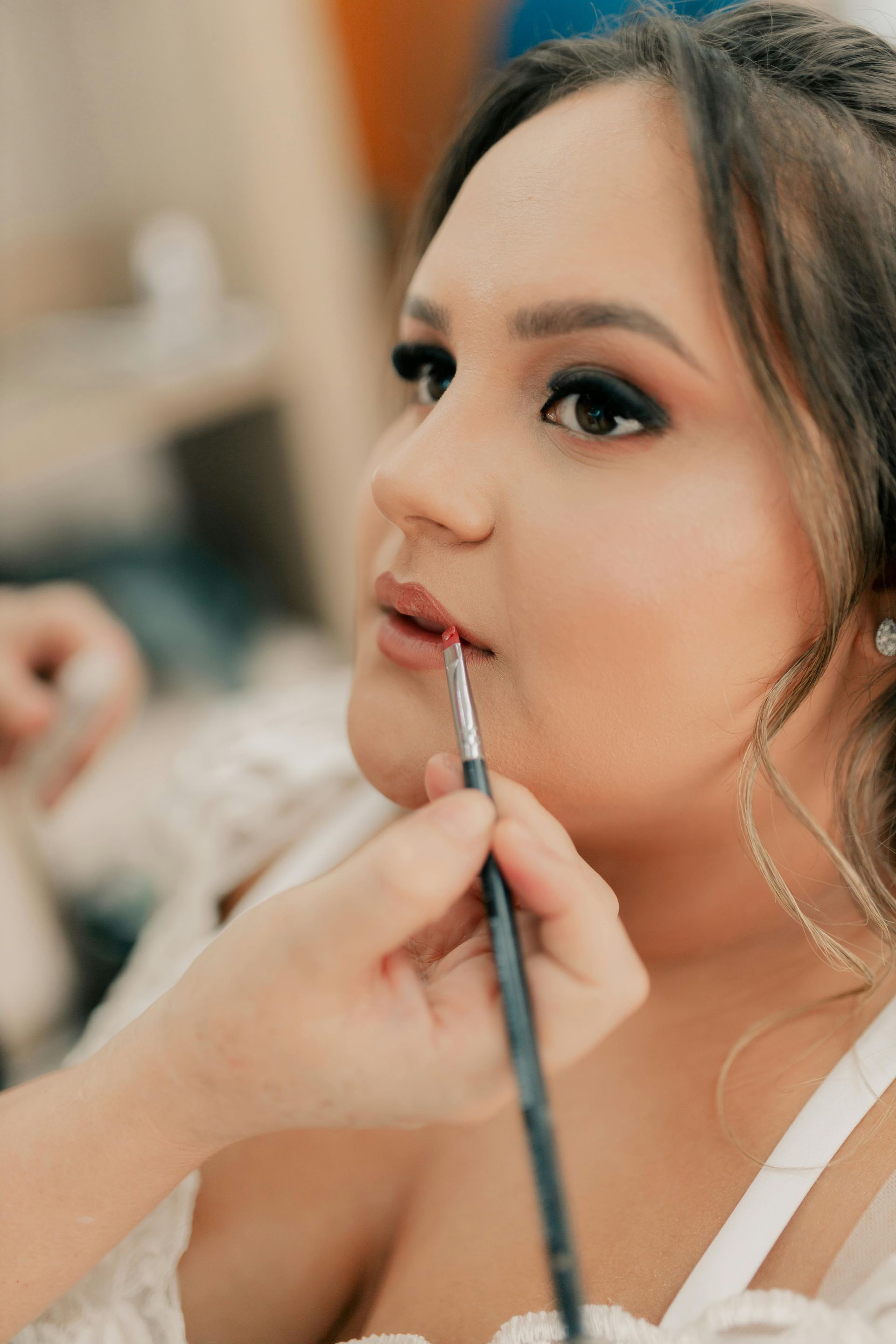 En gros plan, une maquilleuse utilise un pinceau fin pour appliquer soigneusement du rouge à lèvres sur les lèvres d'une cliente.