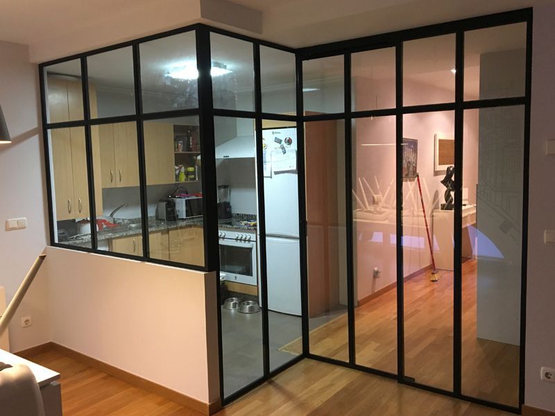 Mampara divisoria moderna de cristal con marco negro y puerta que separa la cocina de la sala de estar contigua
