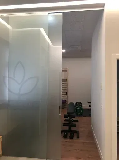 Una puerta corrediza de vidrio esmerilado con el logotipo de una hoja da acceso a un pequeño gimnasio