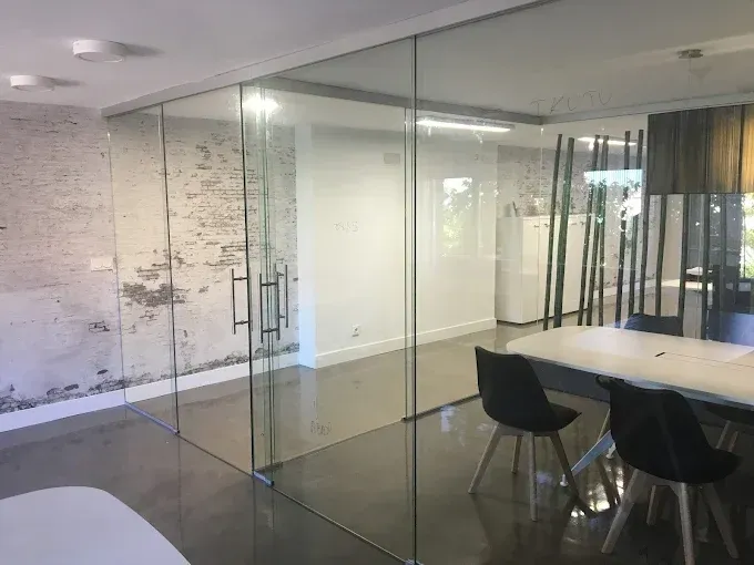 Interior de oficina moderno con una mampara de cristal, suelos de hormigón, pared de ladrillo visto y una mesa con sillas.