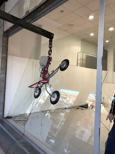 Una herramienta elevadora de vidrio por vacío está suspendida por una grúa, que se acopla a un gran panel de vidrio