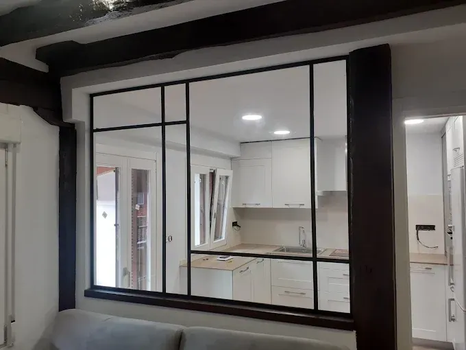 Vista interior de una cocina a través de un separador de ambientes de cristal con marco negro