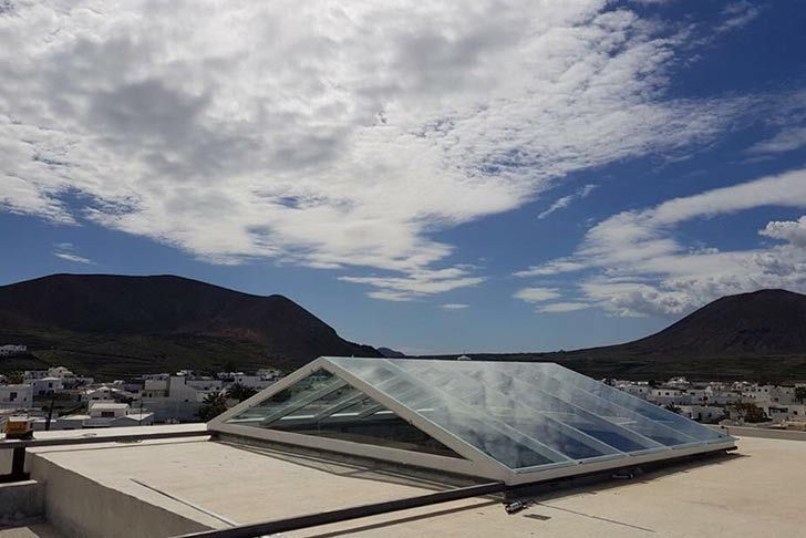 Un tragaluz en el tejado de un edificio con montañas al fondo.