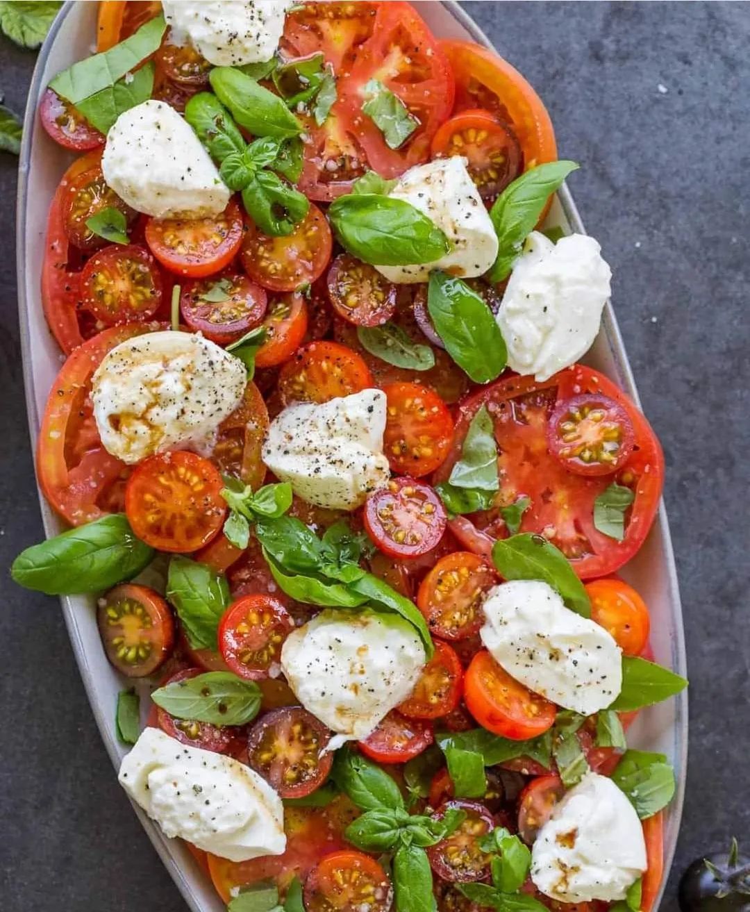 Una ensalada con tomates, mozzarella y albahaca en un plato.