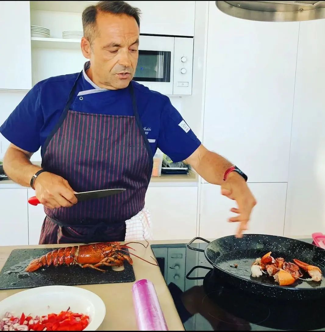Un hombre con delantal está cortando una langosta en una cocina.
