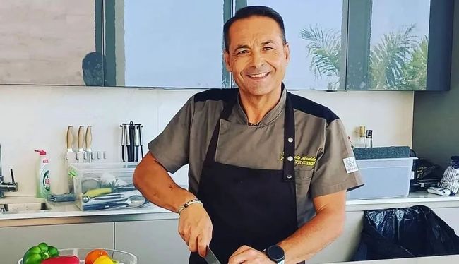 Un hombre con delantal está de pie en una cocina cortando verduras.