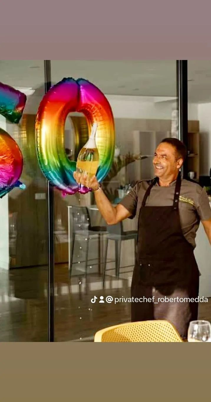 Un hombre con un delantal sostiene un globo de arcoíris con la forma del número 0.