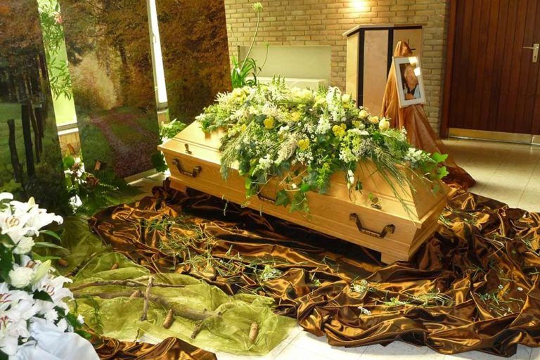 Sarg mit reichhaltiger Blumendekoration in natürlicher Umgebung, umgeben von Pflanzen.