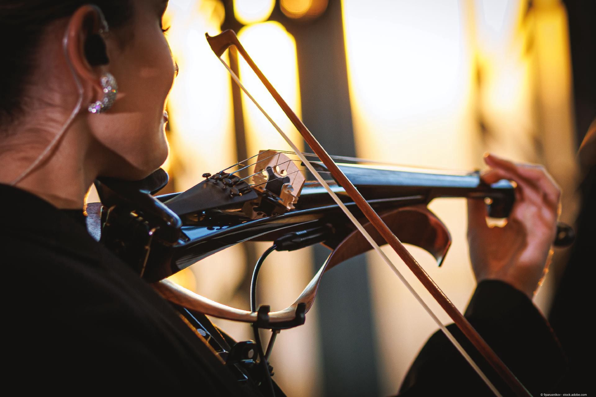 Person spielt Geige in Innenraum, Detailaufnahme von Instrument und Händen.