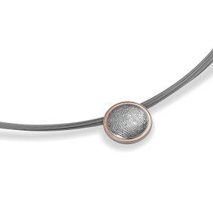 Rundes Schmuckstück mit Fingerabdruckgravur an einer gebogenen Metallspange.