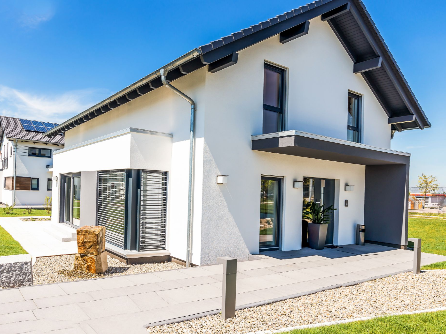 Maison moderne à deux étages avec murs blancs, toit foncé, grandes fenêtres et allée pavée.