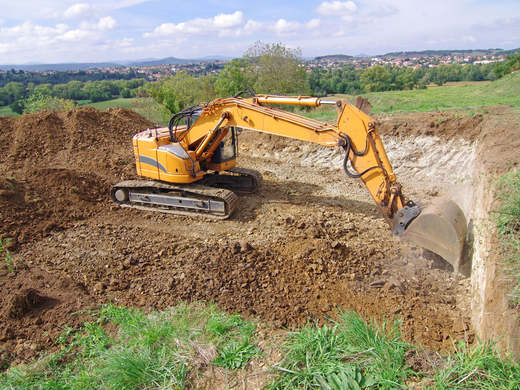 Une pelleteuse jaune creuse une fosse carrée dans un champ.