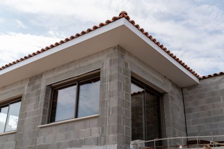 Coin d'un bâtiment en construction, avec des murs en parpaings gris, des fenêtres et un rebord blanc.
