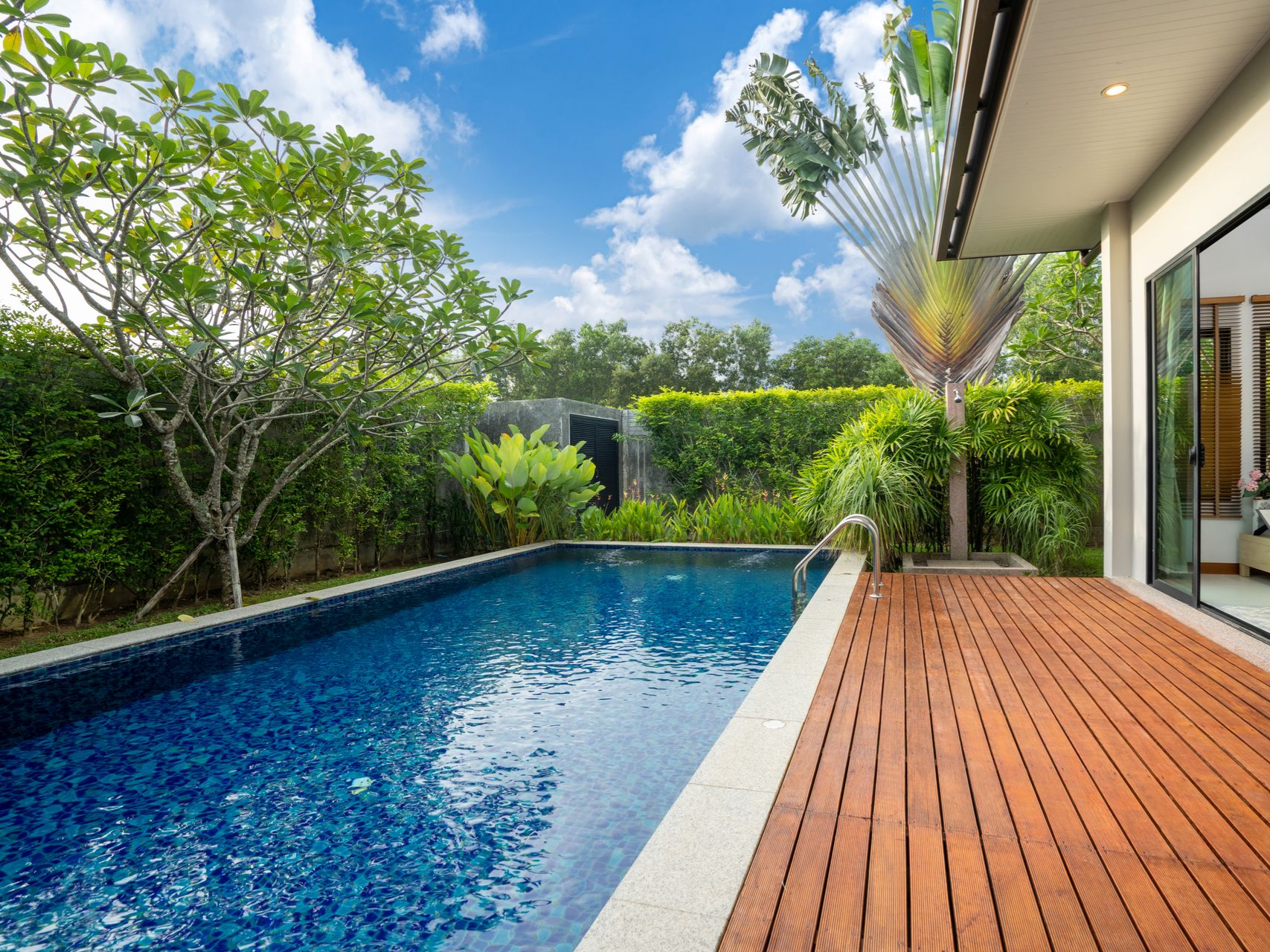 Vue depuis le bord de la piscine, avec des carreaux bleus, une terrasse en bois.