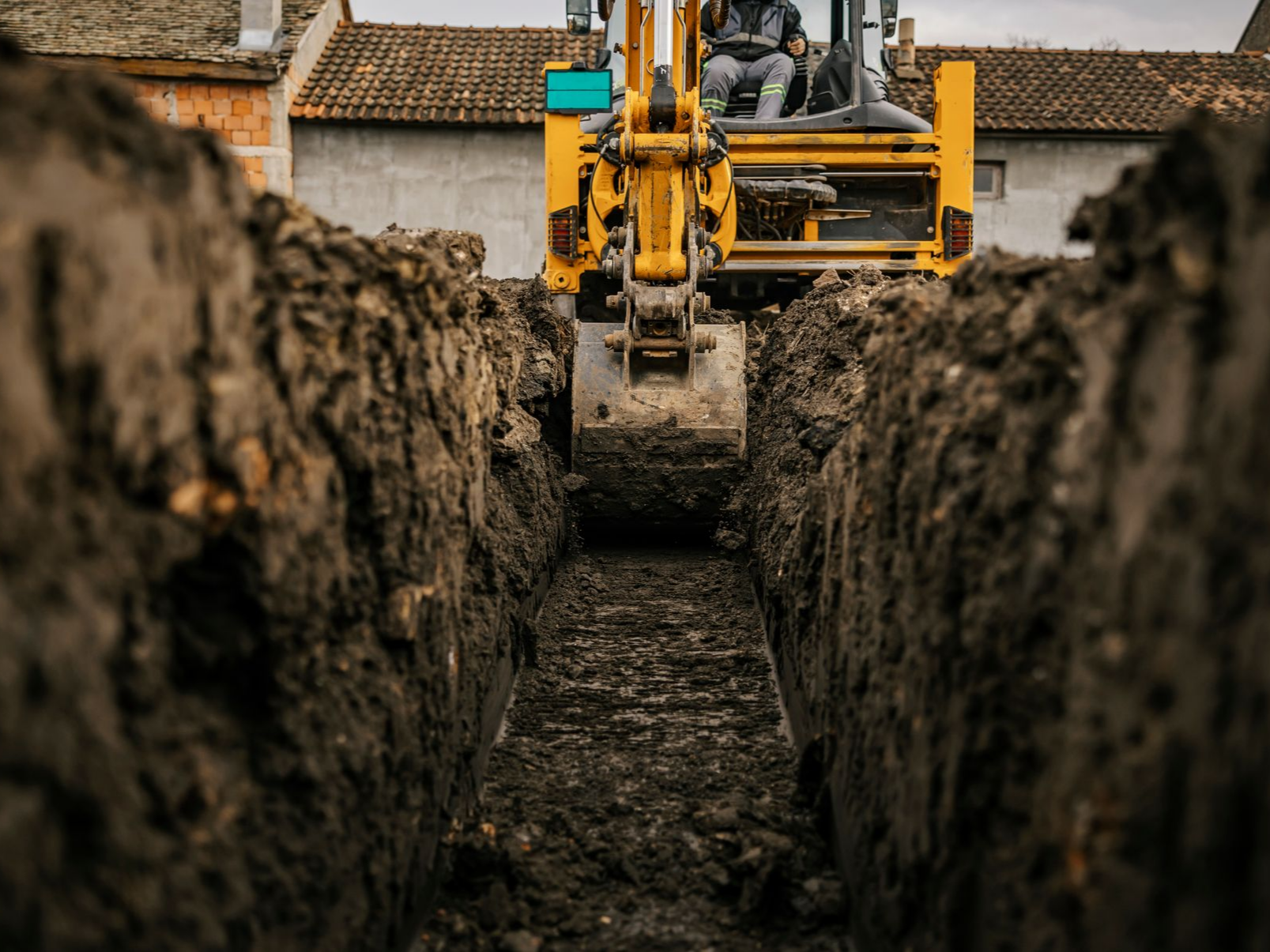 Une pelleteuse jaune creuse une tranchée dans un terrain boueux.