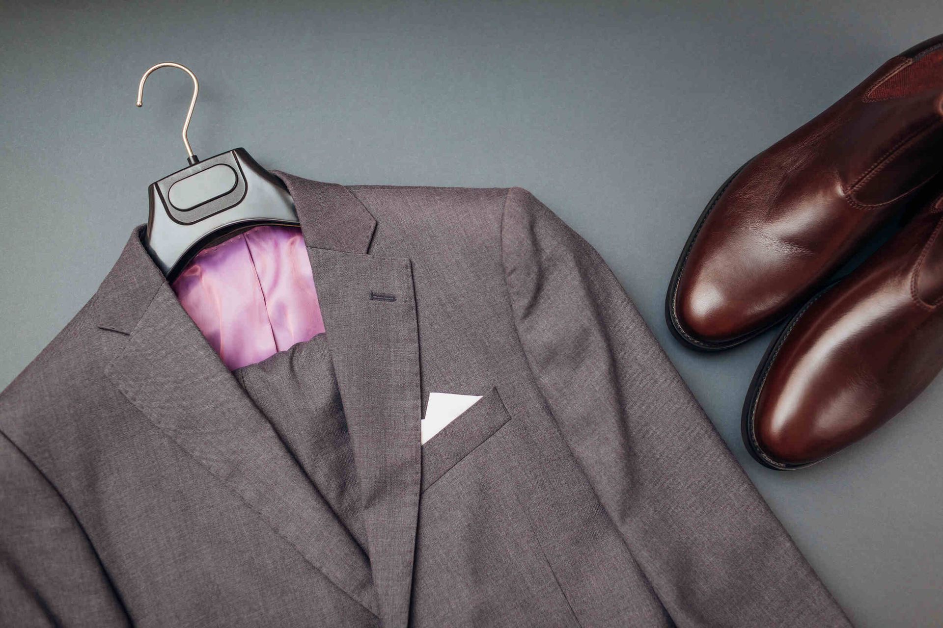 Una chaqueta de traje cuelga en una percha junto a un par de zapatos marrones.
