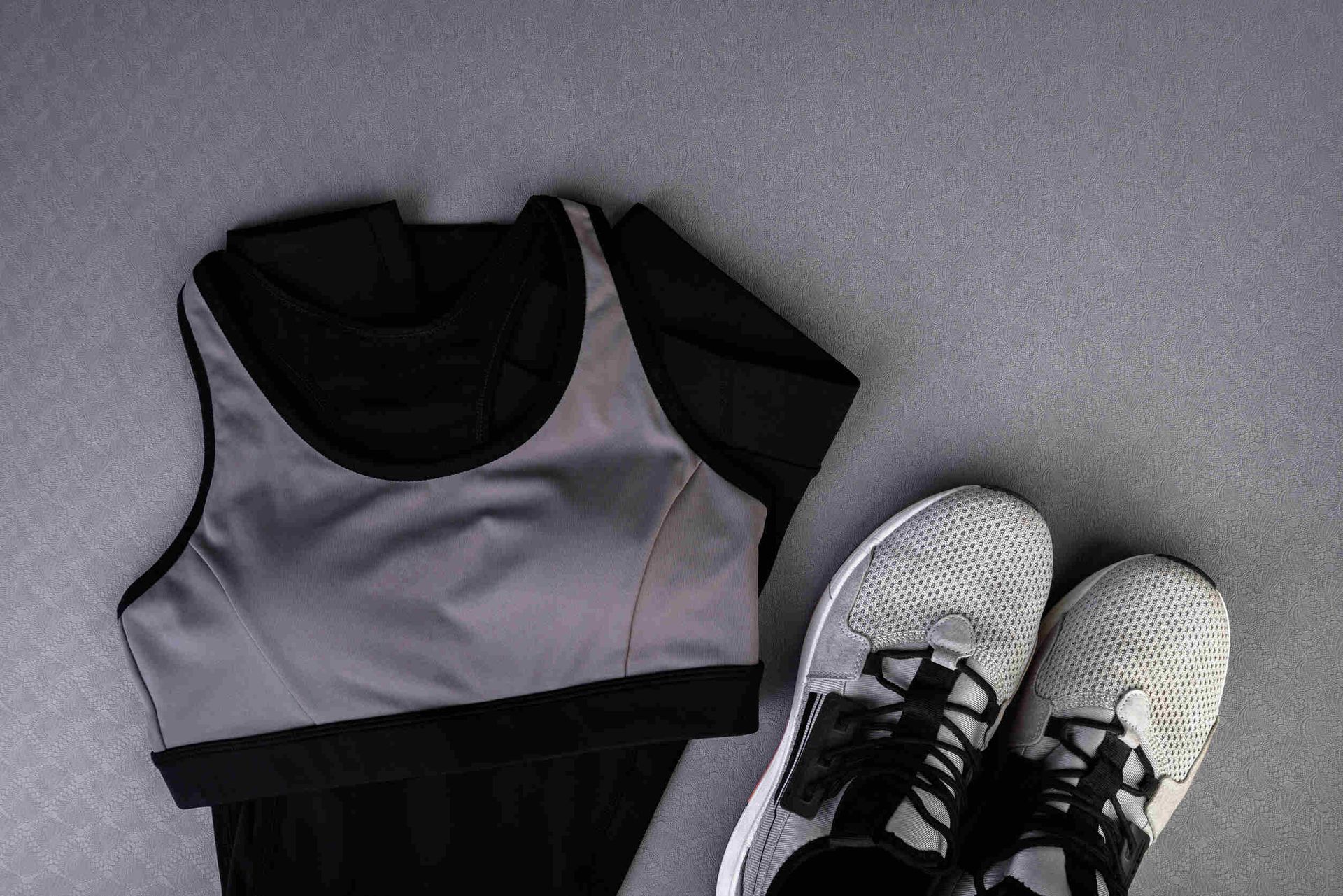 Un par de zapatos, un sujetador deportivo y una camiseta están sobre una superficie gris.
