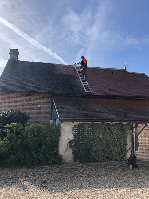 Employé se tenant sur le toit d'une maison en train de nettoyer la toiture